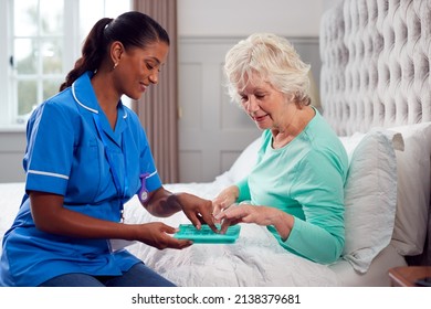 Female Care Worker In Uniform Helping Senior Woman At Home In Bed With Medication