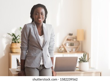 Female Career Concept. Portrait Of Successful Black Businesswoman Standing Near Her Desk In Office And Smiling At Camera, Free Space