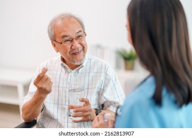 Female Caregiver Giving The Medicine To Her Older Male Patient. Caregiver Nurse Helping Elderly Man Taking Medicine On The Wheelchair At Home.