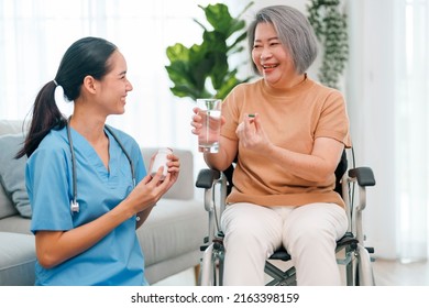 Female Caregiver Giving The Medicine To Her Older Male Patient. Caregiver Nurse Helping Elderly Woman Taking Medicine On The Wheelchair At Home.