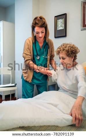 Caregiver helping elderly female patient to get out of bed