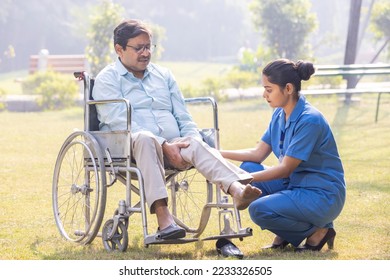 Female caregiver helping senior man in wheelchair to lift lag at park. - Shutterstock ID 2233326505