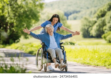 Female caregiver pushing senior woman in wheelchair. Nurse and elderly woman enjoying a warm day in nursing home, public park. - Powered by Shutterstock