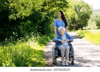 Female caregiver pushing senior woman in wheelchair. Nurse and elderly woman enjoying a warm day in nursing home, public park. - Powered by Shutterstock