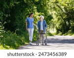 Female caregiver and senior woman with walker on walk in nature. Nurse and elderly woman enjoying a warm day in nursing home, public park.