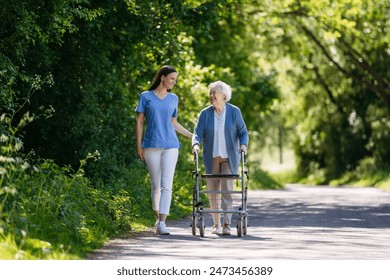 Female caregiver and senior woman with walker on walk in nature. Nurse and elderly woman enjoying a warm day in nursing home, public park. - Powered by Shutterstock