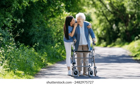 Female caregiver and senior woman with walker on walk in nature. Nurse and elderly woman enjoying a warm day in nursing home, public park. - Powered by Shutterstock