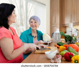 Female caregiver or volunteer and senior adult woman cook vegetable salad together. The old lady looks happy. 