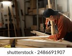 Female Carpenter drilling hole into timber block working in her workshop. Woman doing furniture assembling in studio. Woodworking expert using electric power drill tool. Copy space