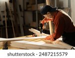 Female Carpenter drilling hole into timber block working in her workshop. Woman doing furniture assembling in studio. Woodworking expert using electric power drill tool. Copy space