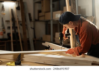 Female Carpenter drilling hole into timber block working in her workshop. Woman doing furniture assembling in studio. Woodworking expert using electric power drill tool. Copy space - Powered by Shutterstock