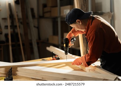 Female Carpenter drilling hole into timber block working in her workshop. Woman doing furniture assembling in studio. Woodworking expert using electric power drill tool. Copy space