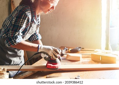 Female carpenter grinding wood with sandpaper in carpentry or diy workshop. Electric sander working in carpentry. Girl polishes wooden board with electric sander. - Powered by Shutterstock