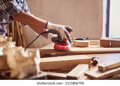 Female carpenter grinding wood with sandpaper in carpentry or diy workshop. Electric sander working in carpentry. Girl polishes wooden board with electric sander.