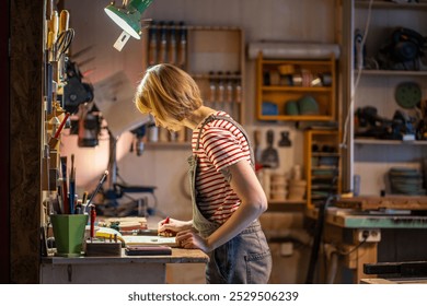 Female carpenter sketching furniture design and projects in woodworking workshop. Craftswoman creating drawing in notebook, small business with furniture assembly, handmade work, creative occupation - Powered by Shutterstock