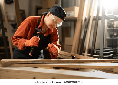 Female carpenter uses chisel to make wood furniture while working in workshop. Copy space - Powered by Shutterstock