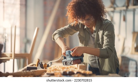 Female Carpenter Wearing Protective Safety Glasses and Using Electric Belt Sander to Work on a Wood Bar. Artist or Furniture Designer Working on a Product Idea in a Workshop. - Powered by Shutterstock