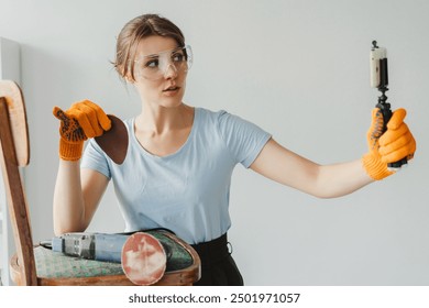 Female carpenter wearing safety goggles holding sandpaper and recording a video blog about furniture renovation using action camera - Powered by Shutterstock