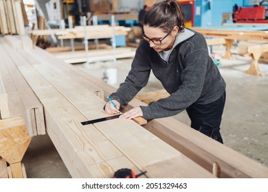 Female Carpenter Working With A Right Angle Tool On A Large Beam Of Timber In An Industrial Woodworking Factory With Copyspace