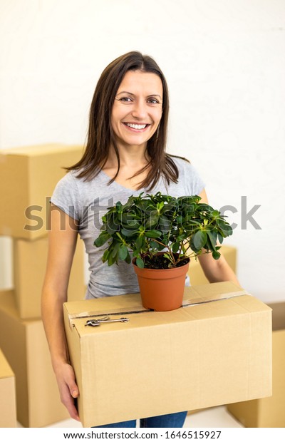 Female carring big carton box packed to be\
delievered to new house and smiles to the camera with beaming\
smile. Concept for buying real\
estate.