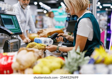 Female cashier scanning groceries with barcode scanner at checkout counter in a supermarket, with a male colleague in the background - Powered by Shutterstock