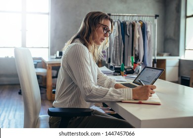 Female in casuals writing in her diary with laptop on desk. E-commerce business owner taking online orders.