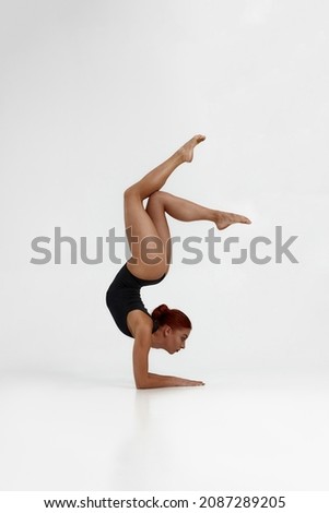 Female caucasian ballet dancer dancing classical ballet dance. Choreography concept. Attractive young flexible girl with red hair barefoot and wearing leotard on white background in studio. Copy space