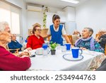 Female caucasian caregiver and senior people in the dining hall of a nursing home