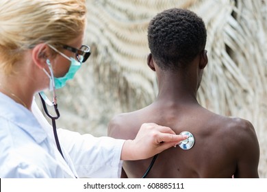 Female Caucasian Doctor Listening Heart Beat And Breathing Of African Black Man Outdoors.Rear View Of Black Man