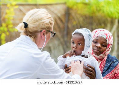 Female Caucasian Doctor Listening Heart Beat And Breathing Of Little African Girl With Stethoscope.Mother Holding The Child