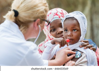 Female Caucasian Doctor Listening Heart Beat And Breathing Of Little African Girl With Stethoscope.Mother Holding The Child