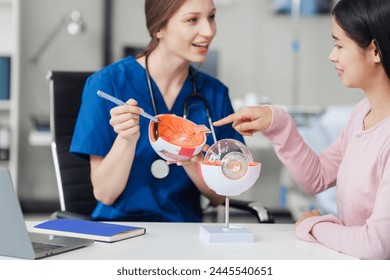 Female Caucasian ophthalmologist explains about eye diseases using the eye model with an Asian female patient At the table in the hospital examination room, Glaucoma, Cataract, Diabetic Retinopathy - Powered by Shutterstock