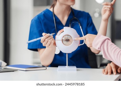 Female Caucasian ophthalmologist explains about eye diseases using the eye model with an Asian female patient At the table in the hospital examination room, Glaucoma, Cataract, Diabetic Retinopathy - Powered by Shutterstock