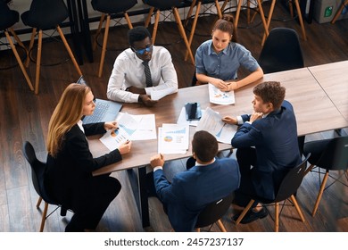 Female CEO leads diverse team in strategy session at modern office, with charts, laptop for data-driven decision making. Professionals engage in creative solutions, collaboration for business growth. - Powered by Shutterstock