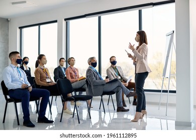 Female CEO Talking To Group Of Business People During Seminar In Board Room. All Of Them Are Wearing Face Masks Due To COVID-19 Pandemic. 