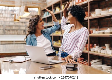 Female ceramists high fiving each other while working together in their store. Cheerful shop owners celebrating their success as a team. Happy young businesswomen running a creative small business. - Powered by Shutterstock
