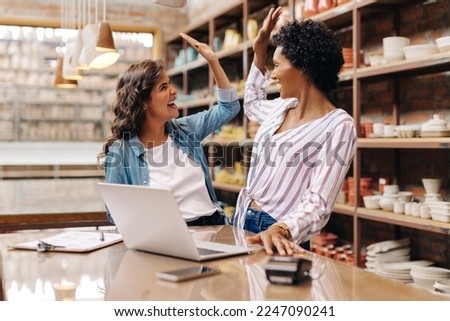 Female ceramists high fiving each other while working together in their store. Cheerful shop owners celebrating their success as a team. Happy young businesswomen running a creative small business.