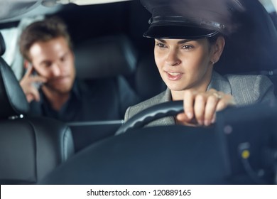 Female Chauffeur Driving A Limousine, Businessman In Background.