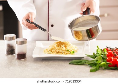 Female Chef Adding White Sauce To Delicious Pasta On Plate