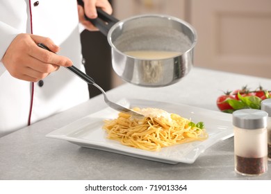 Female Chef Adding White Sauce To Delicious Pasta On Plate