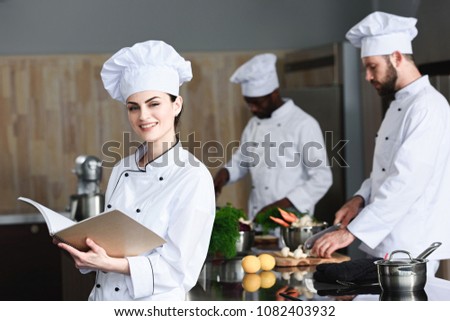 Female chef checking recipe in book by her multiracial colleagues