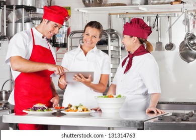 Female chef with colleagues looking for recipe on a tablet computer while cooking at kitchen - Powered by Shutterstock