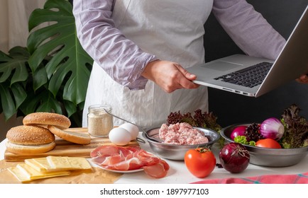 Female Chef Cooking Big Burger Or Cheeseburger And Using Laptop With Cooking Recipe Tutorial.