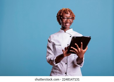 Female chef with digital tablet standing in studio while looking up recipes for new menu items. Head chef with mobile device providing garnish ideas for a gourmet cuisine meal. - Powered by Shutterstock