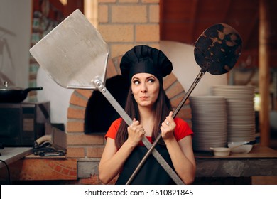 Female Chef in front of Pizza Oven Holding Peels. Cheerful cook standing in a professional restaurant kitchen
