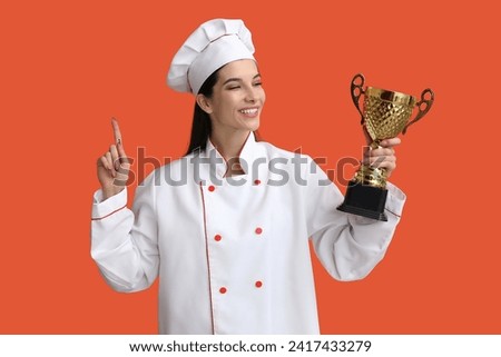 Female chef with gold cup pointing at something on orange background