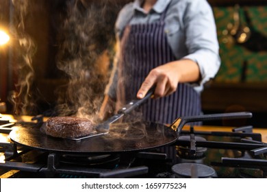 Female chef is grilling juicy, delicious, meat burgers on a kitchen stove in a restaurant. - Powered by Shutterstock