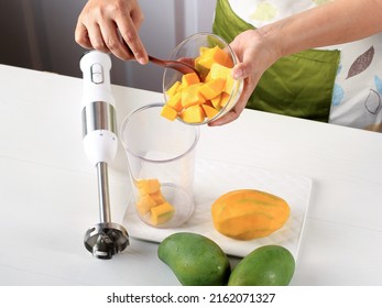 Female Chef Hand Pour Diced Mango To The Juicer Bowl, Process Making Mango Smoothie Or Mango Lassi Juice  In The Kitchen