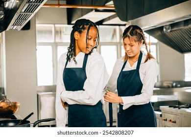 Female chef helps friend tie apron in a restaurant kitchen. Two adults in uniform prepare for food education and service in a professional environment. - Powered by Shutterstock