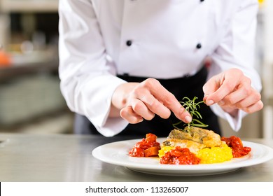 Female Chef in hotel or restaurant kitchen cooking, only hands, she is finishing a dish on plate